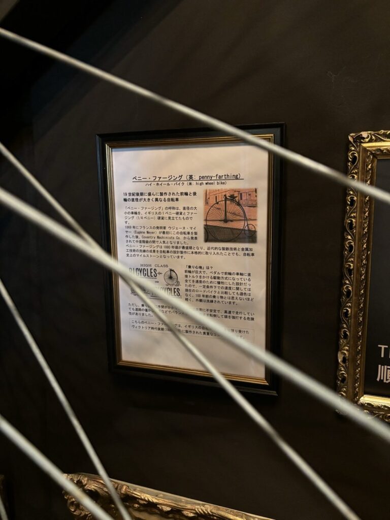 BAM鎌倉のペニー・ファージング（前輪の大きい自転車）の解説パネル。手前に実物の大車輪のスポークが写り、1869年の発明から乗り心地までが日本語で書かれている