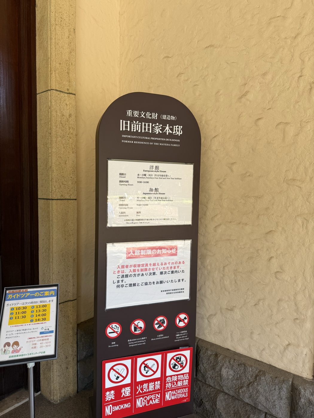 旧前田家本邸の案内板。重要文化財と書かれ、洋館と和館の開館日・開館時間・入館料無料の表示があり、左下にガイドツアーの開始時刻7回を示す案内が立てられている