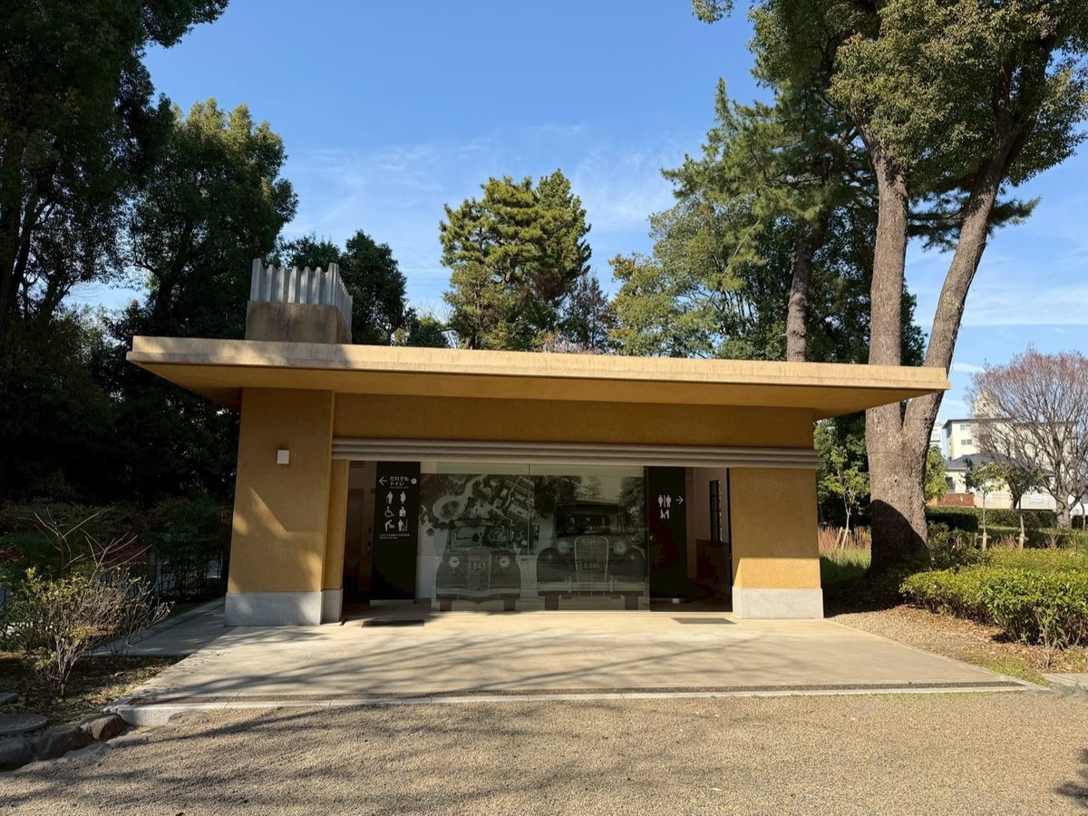 駒場公園にある旧車庫の建物。低い平屋に大きく張り出した庇があり、中央のガラス面に当時の自動車の写真が展示され、左右にトイレのピクトグラムが表示されている