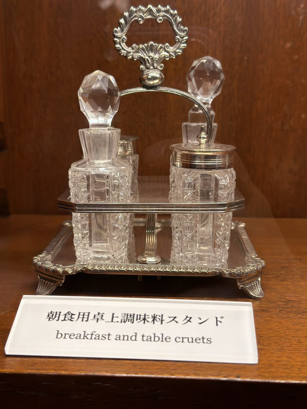 展示されている朝食用卓上調味料スタンド。銀の台にカットガラスの瓶が並び、日英併記のラベルが添えられている