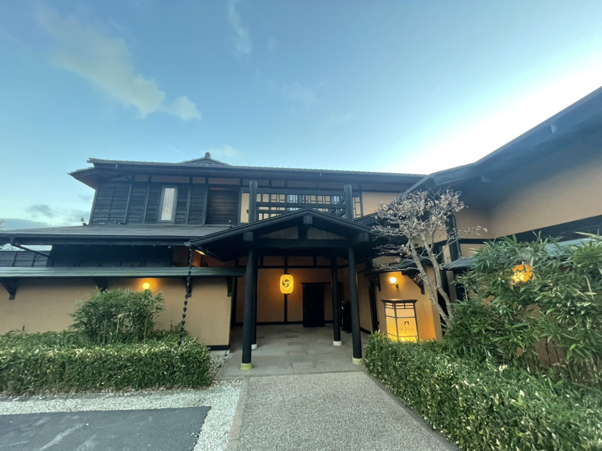 お宿うち山の玄関。夕方の青空の下、玄関の照明がともる和風の門構え