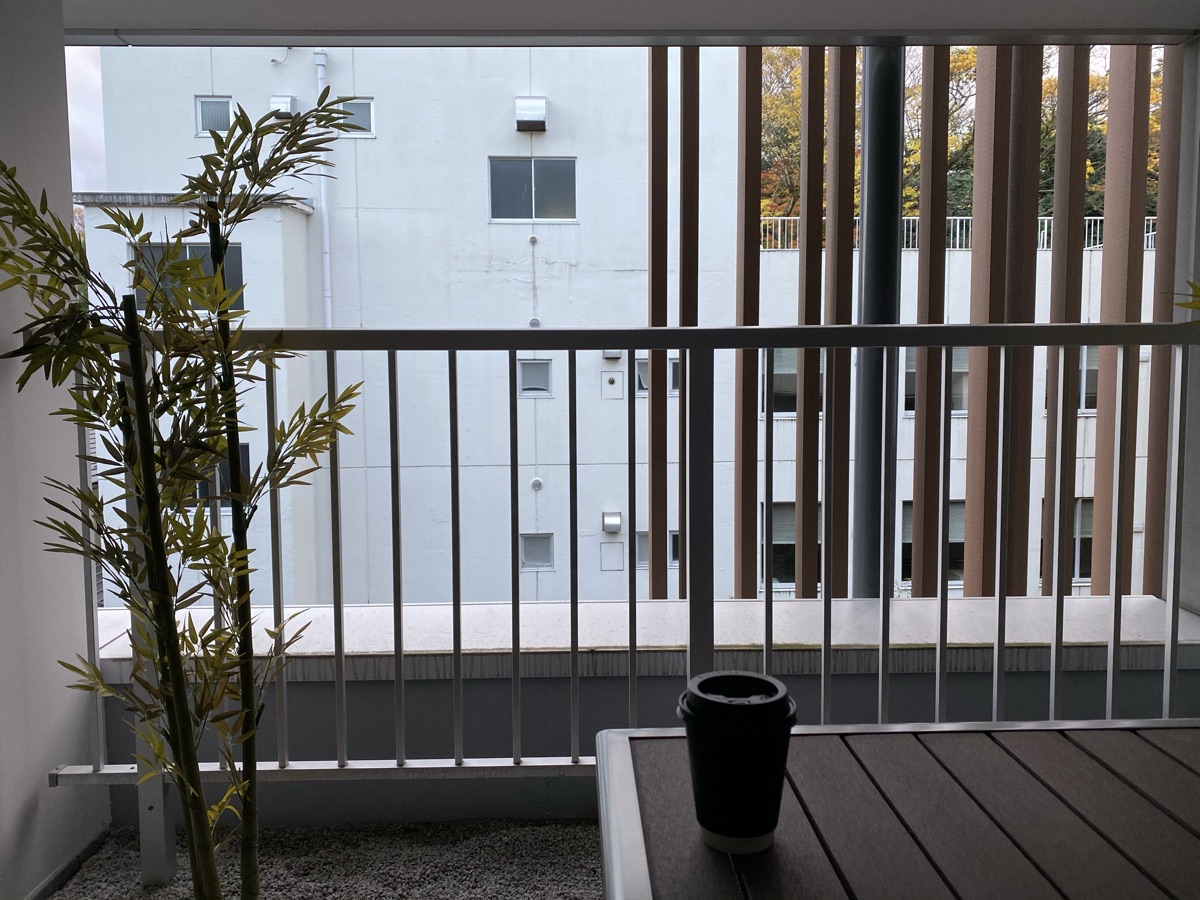 雨庵金沢のテラス席。竹の植栽と木のテーブル、柵の奥に隣の建物と紅葉が見える