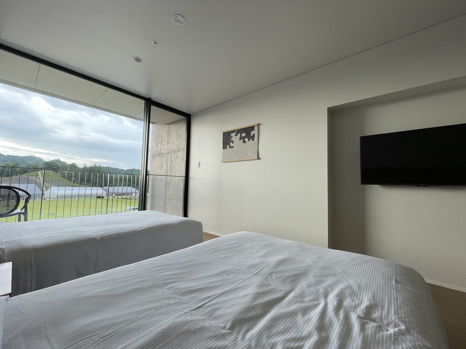 HOTEL VISONのツインの部屋。床から天井までの窓の先にバルコニーと椅子、外に芝生と温室と山(2022年7月)